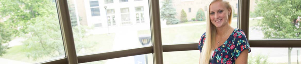 A female student posing at a window at Hilbert College.